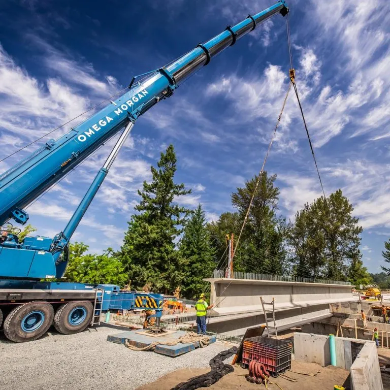 Omega Morgan blue mobile crane lifting concrete bridge beam at construction site